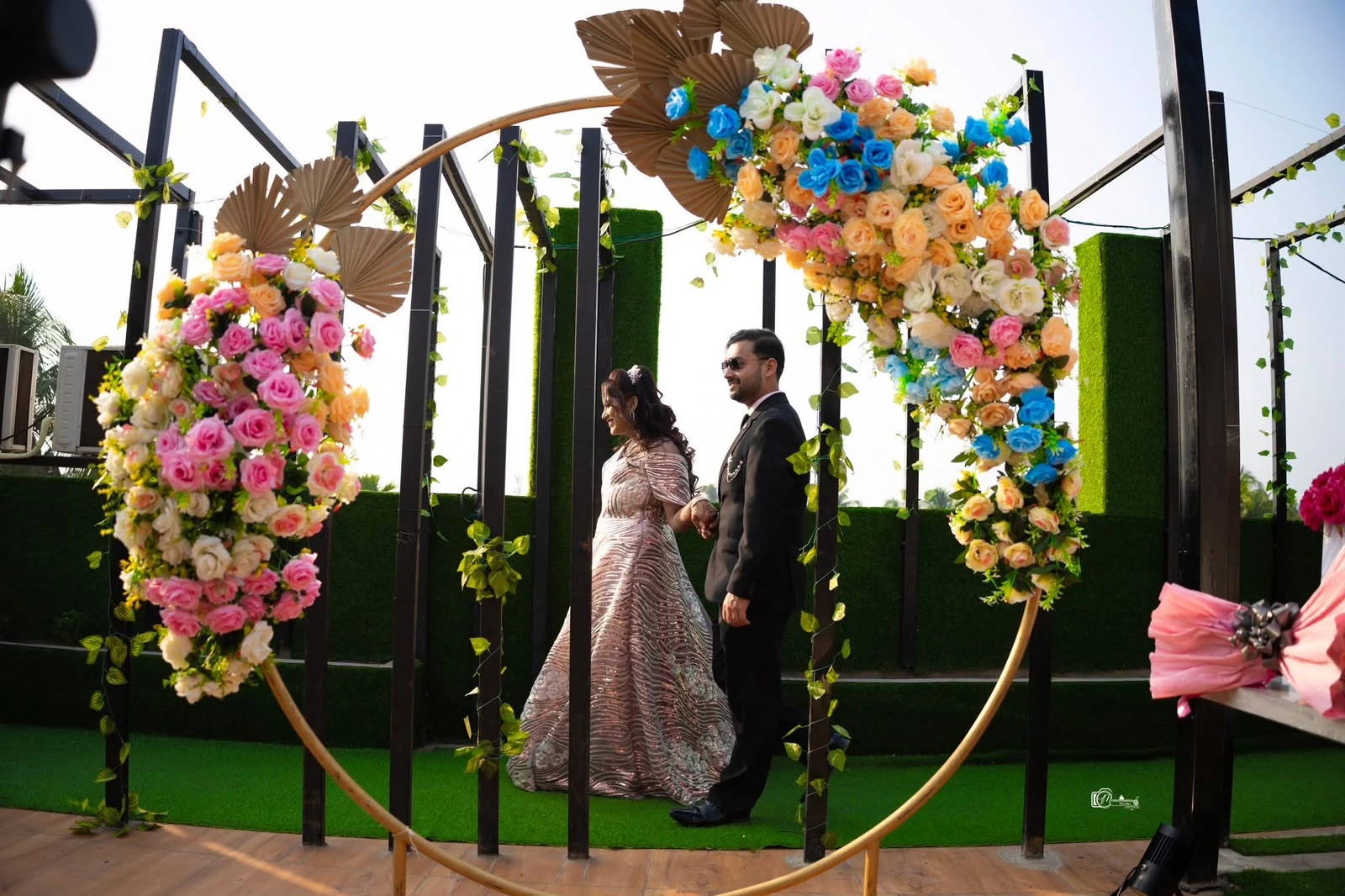 Saheli and Abhishek holding hands beneath a floral arch